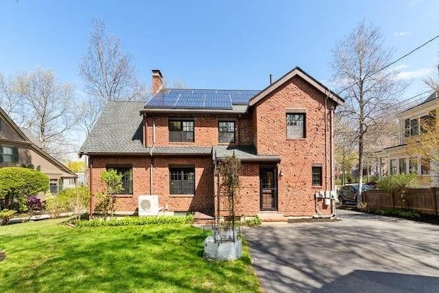 view of front of house with a chimney, brick siding, fence, roof mounted solar panels, and a front lawn