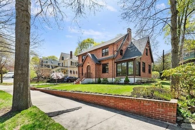 tudor home featuring brick siding, a front lawn, and a chimney