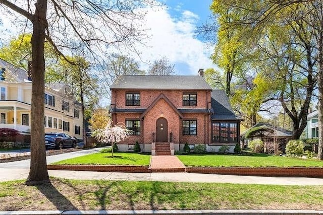 tudor-style house featuring a chimney, a front yard, and brick siding