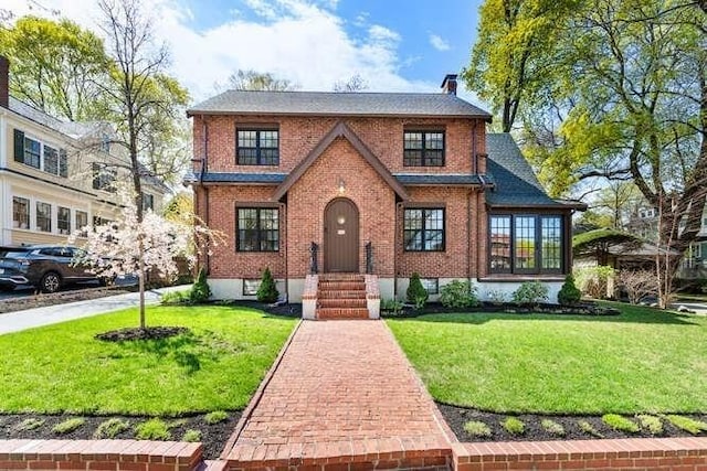 tudor house featuring a chimney, brick siding, and a front yard