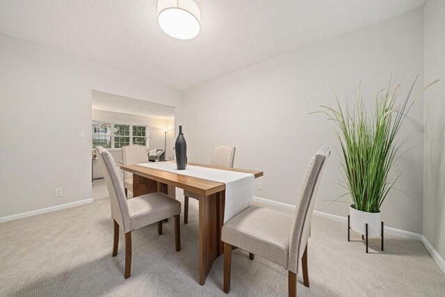 dining space featuring light carpet, baseboards, and a textured ceiling