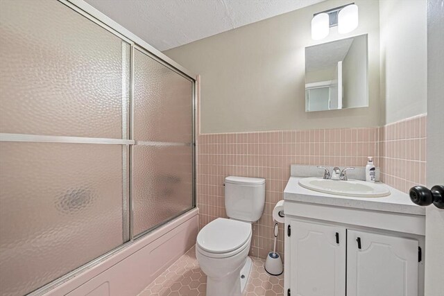 full bath featuring tile walls, tile patterned flooring, toilet, shower / bath combination with glass door, and wainscoting