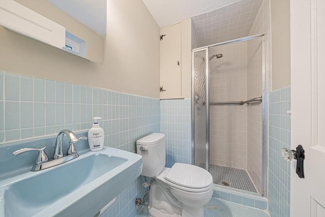 full bath featuring a stall shower, a sink, tile walls, toilet, and a wainscoted wall