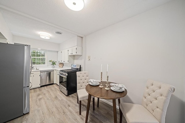 kitchen with appliances with stainless steel finishes, light wood-style flooring, light countertops, a textured ceiling, and white cabinets