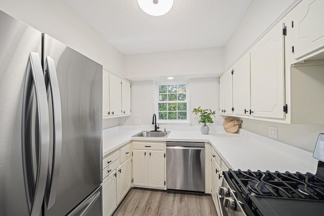 kitchen with appliances with stainless steel finishes, a sink, light wood-style flooring, white cabinets, and a textured ceiling