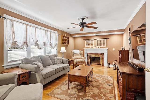 living room with a ceiling fan, a brick fireplace, light wood-style floors, and ornamental molding