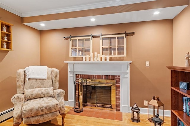 sitting room with a brick fireplace, crown molding, a baseboard heating unit, baseboards, and wood finished floors