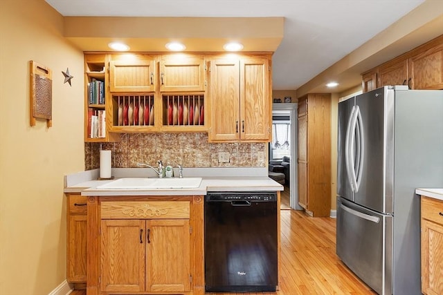 kitchen featuring backsplash, light countertops, black dishwasher, freestanding refrigerator, and a sink