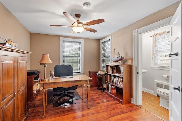 home office with baseboards, radiator, a ceiling fan, and light wood finished floors