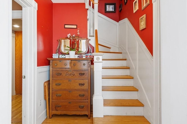 stairway with wainscoting and wood finished floors