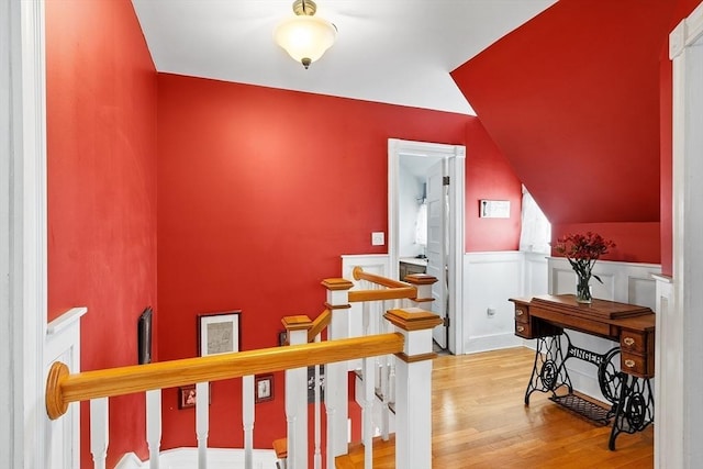 staircase with a wainscoted wall, lofted ceiling, and wood finished floors