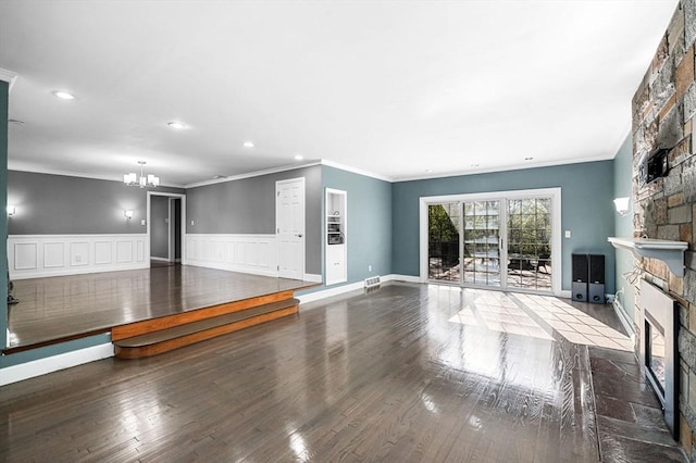 unfurnished living room featuring a stone fireplace, ornamental molding, wood finished floors, and a chandelier