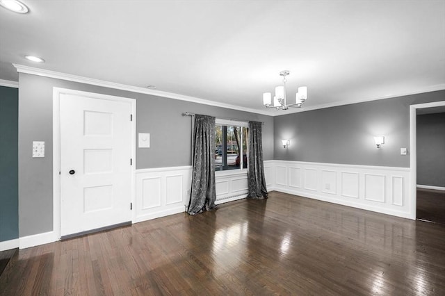 empty room with crown molding, a wainscoted wall, wood finished floors, and a chandelier