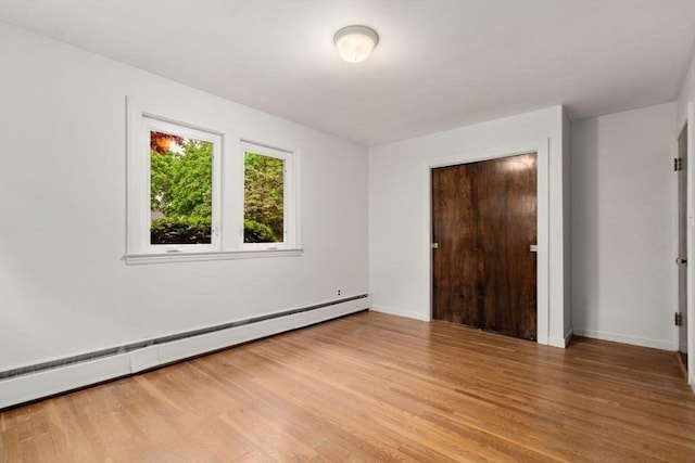 unfurnished bedroom with baseboard heating, light wood-type flooring, and baseboards