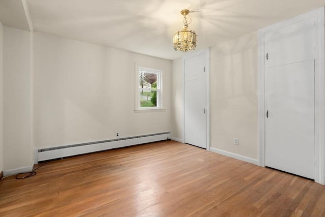 unfurnished bedroom with baseboard heating, a chandelier, light wood-style flooring, and baseboards