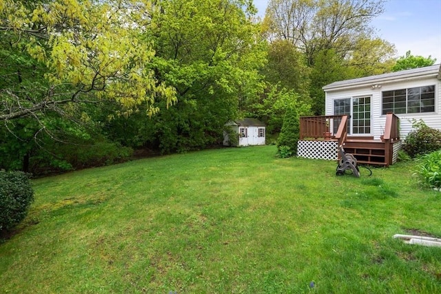 view of green lawn with a shed, a wooden deck, and an outbuilding