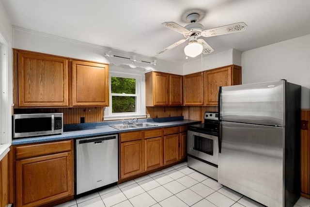 kitchen featuring appliances with stainless steel finishes, a sink, brown cabinets, a ceiling fan, and light tile patterned flooring