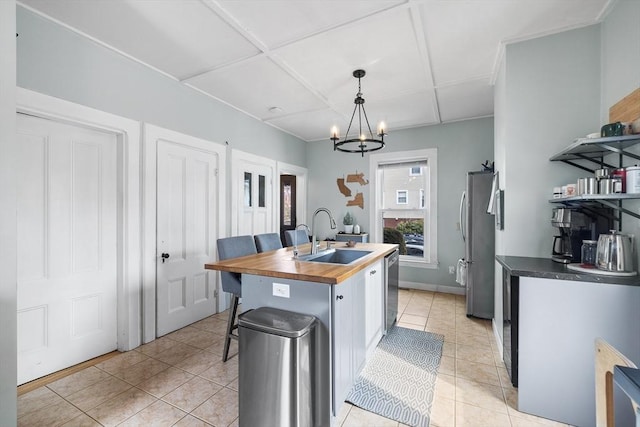 kitchen with sink, wooden counters, decorative light fixtures, a center island with sink, and stainless steel appliances