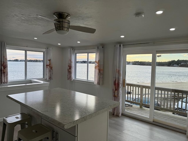 kitchen with recessed lighting, a breakfast bar, a water view, light wood-style floors, and a center island