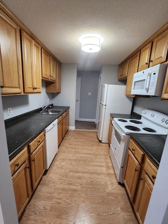 kitchen with light wood-type flooring, a textured ceiling, sink, and white appliances