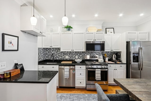 kitchen featuring crown molding, white cabinetry, stainless steel appliances, and hanging light fixtures