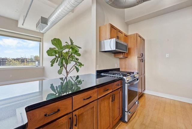 51 Lafayette St Unit 304, Salem, MA 01970 - kitchen featuring white microwave, gas stove, brown cabinetry, light wood finished floors, and dark stone counters