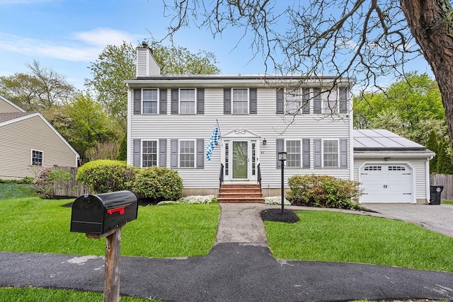 colonial inspired home with a garage, a chimney, a front yard, and entry steps