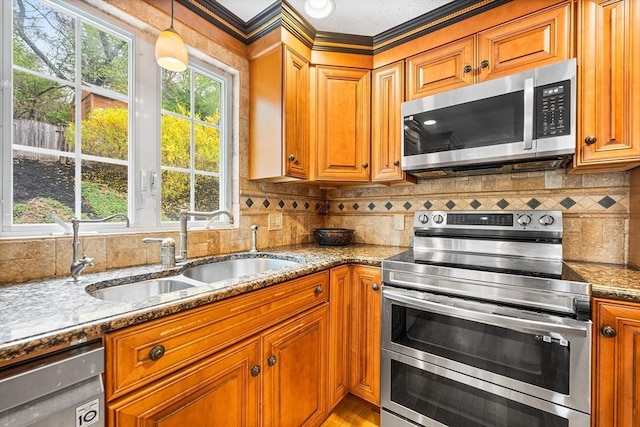 kitchen with appliances with stainless steel finishes, a sink, stone countertops, brown cabinetry, and backsplash