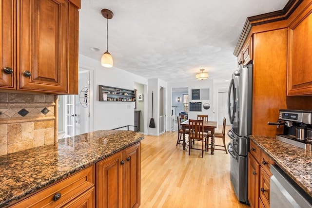 kitchen with stainless steel appliances, brown cabinetry, light wood-type flooring, decorative backsplash, and dark stone counters