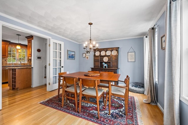 dining room with light wood-style flooring, a chandelier, baseboards, crown molding, and french doors