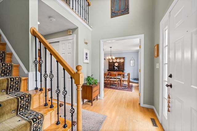foyer with light wood-style floors, stairs, a chandelier, baseboards, and a high ceiling