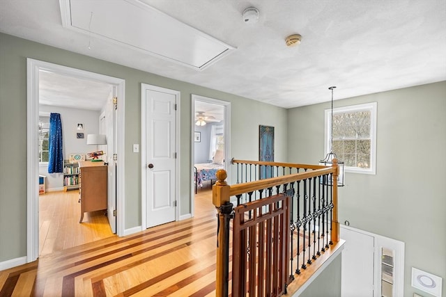 corridor with attic access, light wood-style floors, an upstairs landing, and baseboards