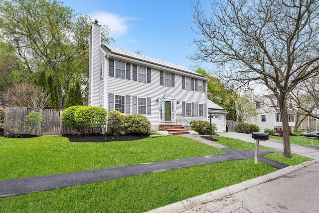 colonial house featuring a chimney, asphalt driveway, and an attached garage