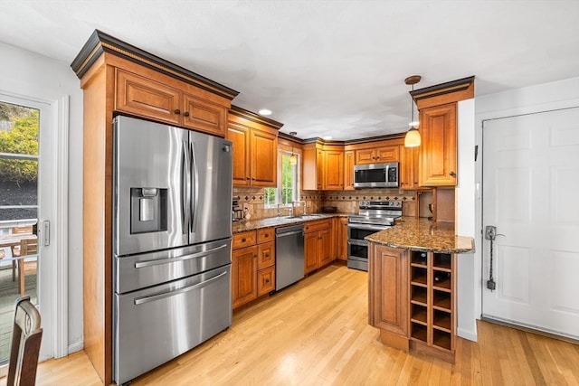 kitchen featuring stainless steel appliances, a sink, brown cabinetry, light wood-style flooring, and dark stone countertops