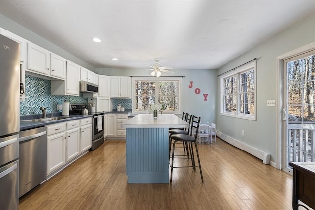 kitchen featuring a baseboard radiator, white cabinets, appliances with stainless steel finishes, a kitchen island, and a breakfast bar