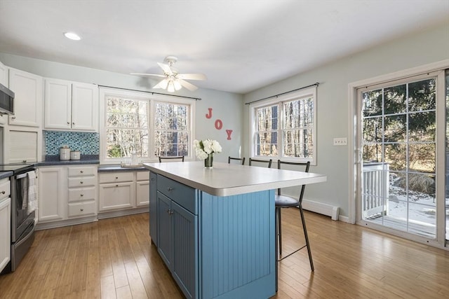 kitchen with appliances with stainless steel finishes, white cabinetry, tasteful backsplash, light hardwood / wood-style flooring, and blue cabinets