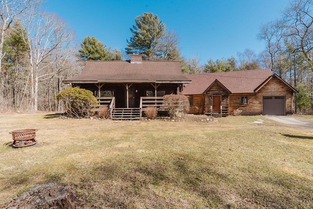 log-style house featuring driveway, an outdoor fire pit, a chimney, roof with shingles, and an attached garage