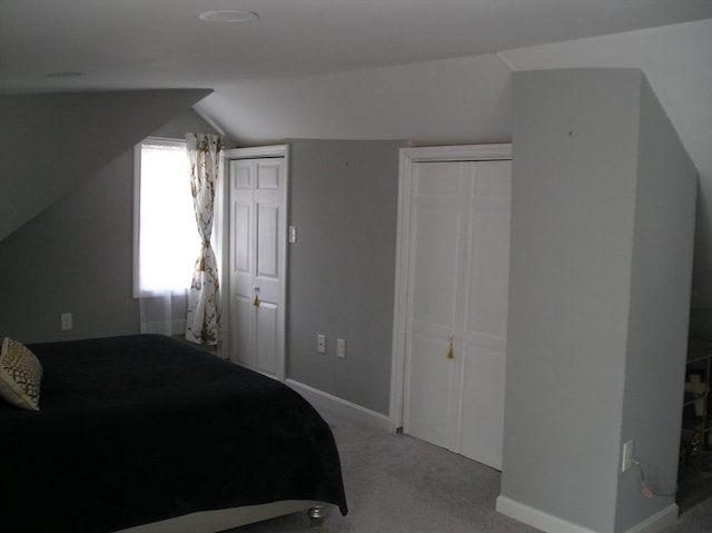 bedroom with lofted ceiling, multiple closets, and light colored carpet