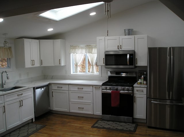 kitchen with appliances with stainless steel finishes, lofted ceiling with skylight, white cabinets, and sink