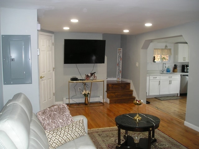 living room with baseboard heating, sink, electric panel, and hardwood / wood-style flooring