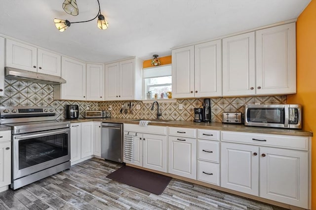 kitchen with a sink, appliances with stainless steel finishes, under cabinet range hood, and white cabinetry