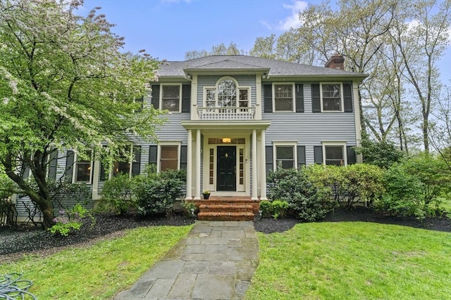 view of front facade with a chimney, a front yard, and a balcony