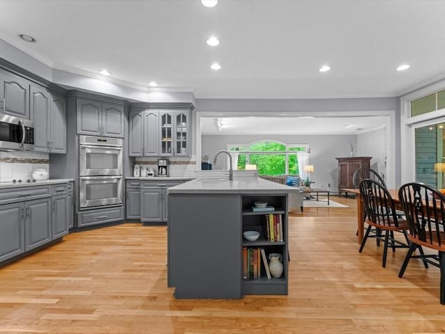 kitchen with gray cabinetry, appliances with stainless steel finishes, a sink, crown molding, and tasteful backsplash
