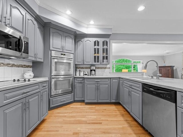 kitchen featuring gray cabinetry, stainless steel appliances, a sink, crown molding, and tasteful backsplash