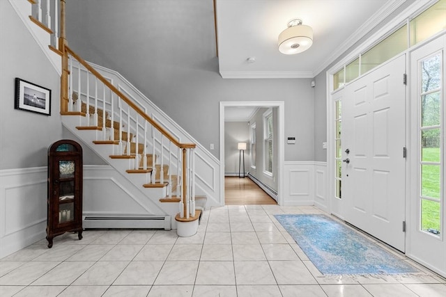 entryway with baseboard heating, ornamental molding, a decorative wall, a wainscoted wall, and stairs