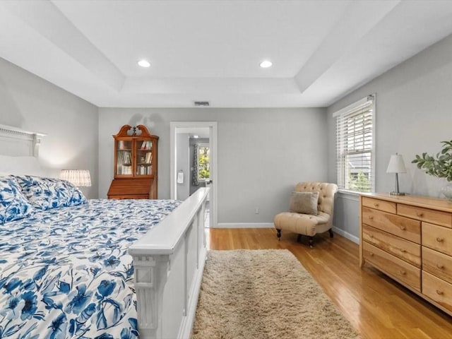 bedroom featuring light wood-style floors, a tray ceiling, multiple windows, baseboards, and recessed lighting