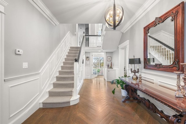 foyer entrance featuring a chandelier, crown molding, stairway, and a decorative wall
