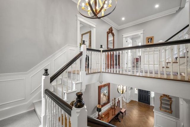 stairs with ornamental molding, a notable chandelier, a decorative wall, and wainscoting