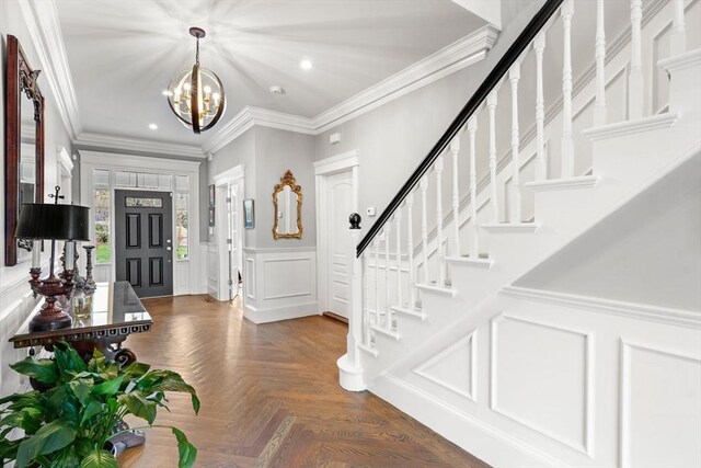 foyer entrance featuring stairs, a decorative wall, ornamental molding, recessed lighting, and a chandelier