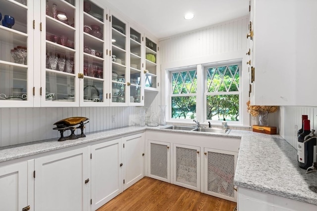 kitchen with white cabinets, light stone countertops, light wood-type flooring, and sink